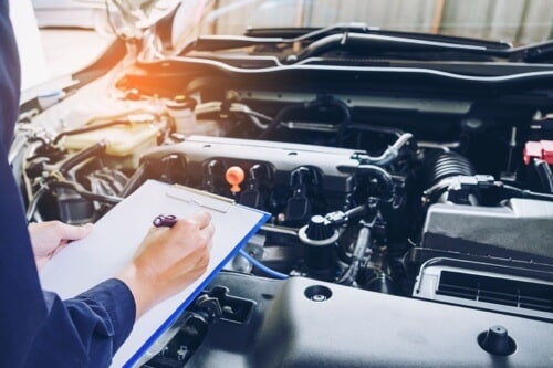 Your Guide to Scheduled Vehicle Maintenance Repair One in The Woodlands and Klein Tx. image of mechanic with checklist inspecting engine
