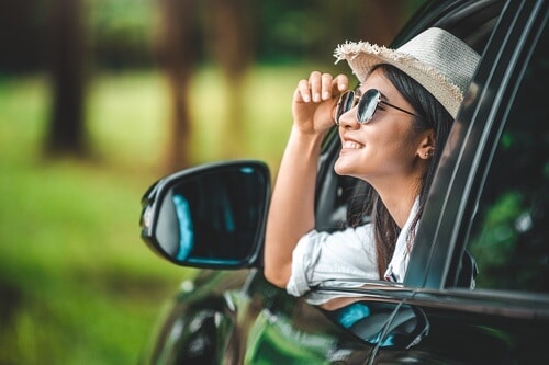 Top 5 Tips For Staying Safe On All Your Travels with Repair One in The Woodlands Tx and Spring/Klein Tx image of happy young woman with sunglasses and summer hat on looking out driver side window smiling