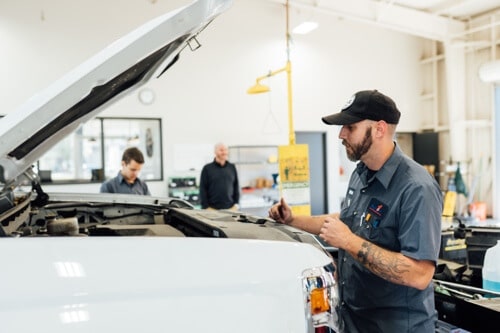 Why Vehicle Maintenance Should Always Start with an Inspection with Repair One Auto in Klein, TX image of mechanic working on white pick up truck with the hood open in shop bay