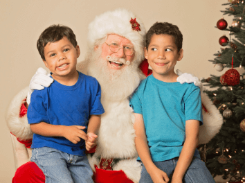 Toys For Tots Donation Location at Repair One in the Woodlands and Klein TX. image of 2 boys making silly faces while sitting on a smiling Santa's lap