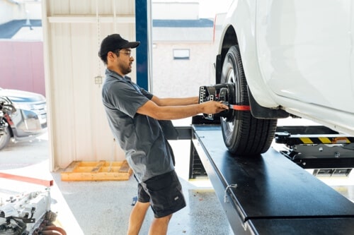How Often Do Drivers In Klein, TX Know Wheel Alignment Is Needed? with Repair One Auto; image of mechanic adjusting alignment machine to white sedan tire that is on alignment machine in shop
