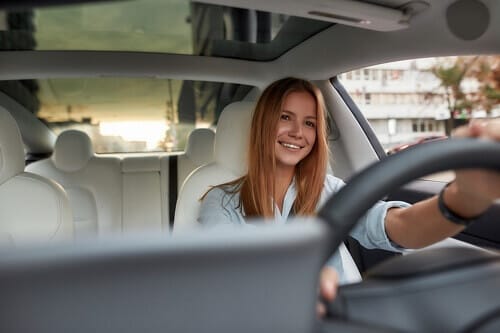Will an Alignment Fix a Crooked Steering Wheel in The Woodlands, TX? with Repair One Auto. Image of red head middle aged woman smiling while driving in her car