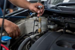 3 Chilling Reasons to Have A/C Repair & Service | Repair One in Klein TX. Closeup image of an auto mechanic checking and fixing a car air conditioner system in a garage.