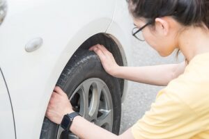 Symptoms of Bad Wheel Alignment | Repair One in Spring, TX. Closeup image of a young woman checking her car tire and worrying about something’s wrong with her wheel.