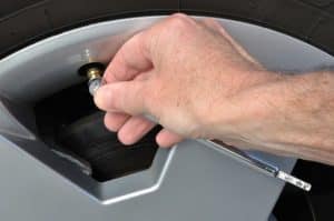 When Should Tires Be Checked and Serviced? | Repair One in Spring, TX. Closeup image of a mechanic’s hand checking the air pressure of a tire with a tire pressure gauge.