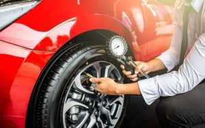 More or Less Tire Pressure: Which is Better? | Repair One in Klein, TX. Image of a man holding pressure gauge to measure air quantity of his inflated car tires.