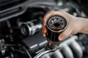 Do I Need an Oil Change & Oil Filter Change Before the Cold Months? | Repair One Auto in The Woodlands, TX. Closeup image of an old oil filter of car with wrench in hand. Concept image of oil and oil filter change.