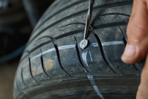 Repair or Replace a Flat Tire—Which is Better? | Repair One in Sprin/Klein, TX. Image of a mechanics’ hand fixing a car's tire by trying to remove nail from hole.