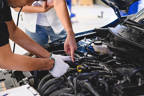 A Reliable Vehicle Is More Than Just Luck! | Repair One in The Woodlands, TX. Image of a male auto mechanic examining a car engine in front of a female customer.