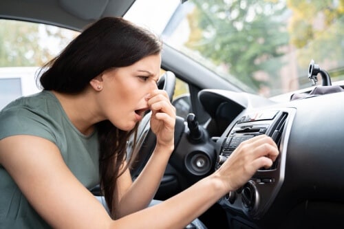 Woman noticing bad smell from air conditioning system. Concept image of “4 Common Signs That Your Vehicle Has AC Problems” | Repair One in Klein & Spring, TX.