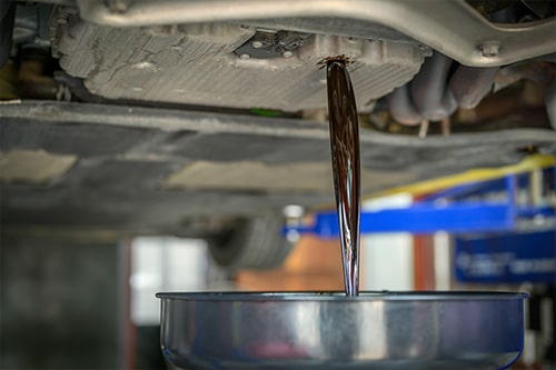 Old, used engine oil flowing out into an engine oil pan. Concept image of “How Oil Change Affects Your Car's Performance” | Repair One in The Woodlands, TX.