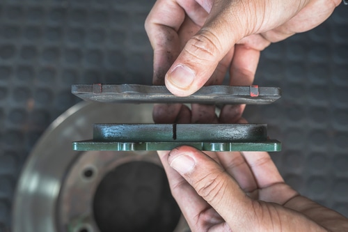 Brake pad and Brake rotor replacement near me in the Woodlands, TX with Repair One. Image mechanic holding old brake pad over new brake pad to show the difference between the two.