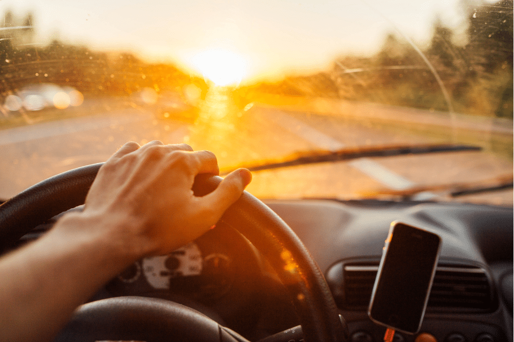 car maintenance, auto repair in The Woodlands, TX at Repair One Tire & Auto. Driving toward the setting sun with visible glare through a dirty windshield, highlighting the need for clean glass and safe driving conditions.