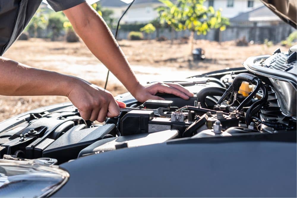 car maintenance, auto repair in The Woodlands, TX at Repair One Tire & Auto. Mechanic working under the hood of a car, using a tool while leaning on the engine bay in an outdoor setting.
