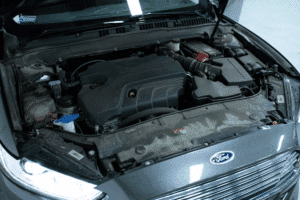 Why Texas Drivers Should Check Their Brakes Before Spring Rain Hits 3 Fall Car Care, auto repair in The Woodlands, TX at Repair One Tire & Auto. Mechanic working under the hood of a car, using a tool while leaning on the engine bay in an outdoor setting.