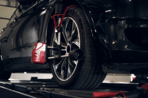National Car Care Month: Vehicle Inspection in The Woodlands, TX 2 Uneven Tire Wear: Vehicle wheel and tire being inspected with a tire alignment measuring tool in an auto repair shop.